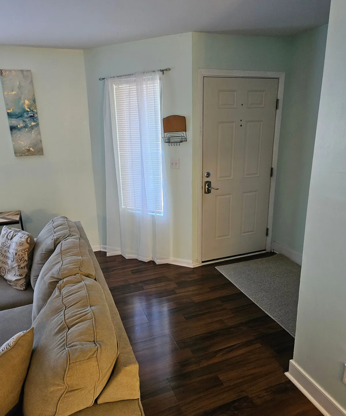 This image displays a cozy living area with a sofa positioned near the entry door and a window, capturing the immediate impression upon entering the apartment. The space feels welcoming and provides a sense of arrival and comfort, with soft lighting and simple, modern décor.