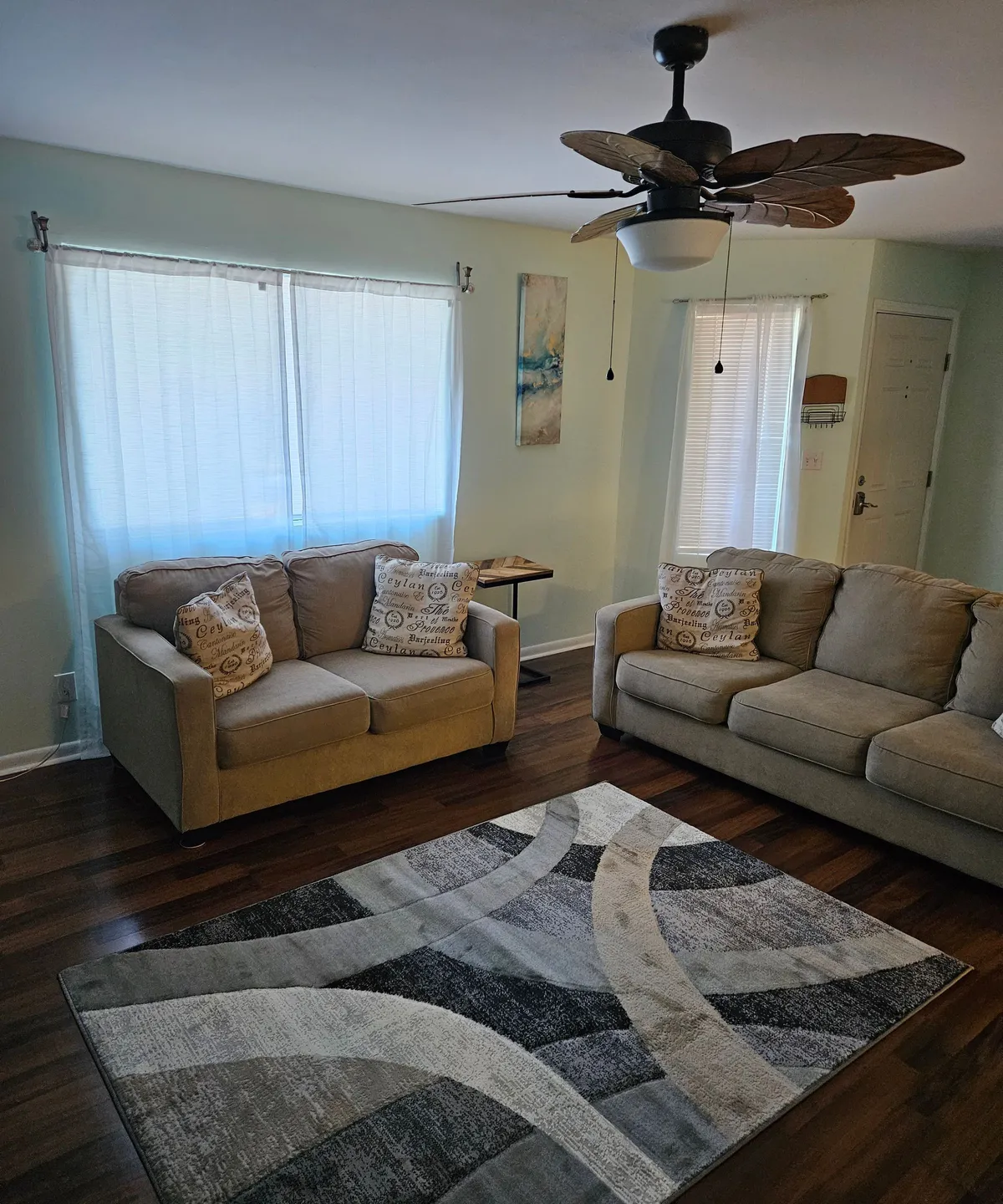 A stylish living area featuring plush sofas, a soft rug, ceiling fan, and tasteful artwork. The arrangement exudes a modern, comfortable vibe and showcases upgraded furnishings, reinforcing the welcoming ambiance of the apartment's interior.