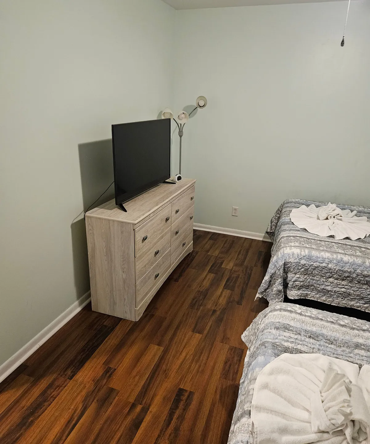 This image highlights a cozy bedroom with two beds, a dresser, and a television. The arrangement suggests opportunities for shared moments, such as watching movies together after a day out, and provides a sense of home-like comfort and relaxation.