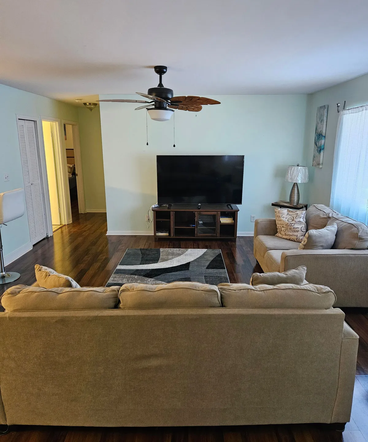 A cozy living area featuring a comfortable sofa set arranged around a television, complemented by a ceiling fan above and decorative art on the walls. The space feels inviting and is ideal for socializing or relaxing after a day of adventures.