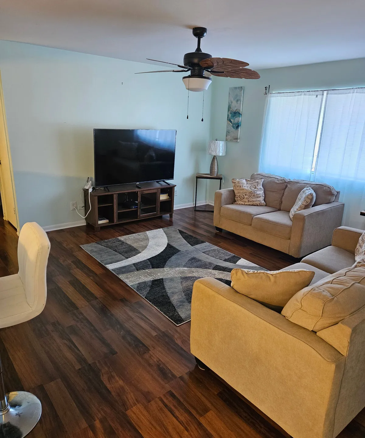 The image showcases a warm, inviting living room featuring a plush sofa, stylish rug, soft lighting from a contemporary lamp, and a large television. The setting exudes comfort and is perfect for relaxing, socializing, or enjoying entertainment with friends and family. Modern touches and tasteful decor create a welcoming ambiance.